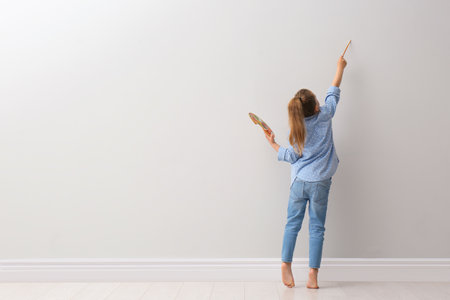 Little girl painting on light gray wall indoors, back view. Space for textの写真素材