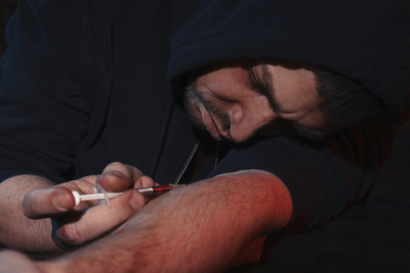 Addicted man taking drugs on dark backgroundの写真素材