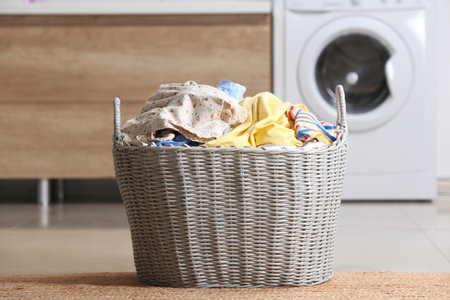 Wicker basket with dirty clothes on floor in laundry roomの写真素材