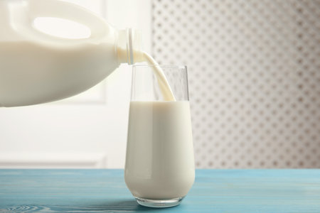 Pouring milk from gallon bottle into glass on blue wooden tableの写真素材