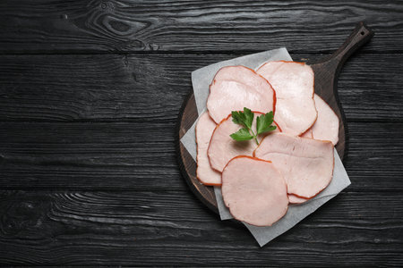 Delicious cut ham with parsley on black wooden table, top view. Space for textの写真素材