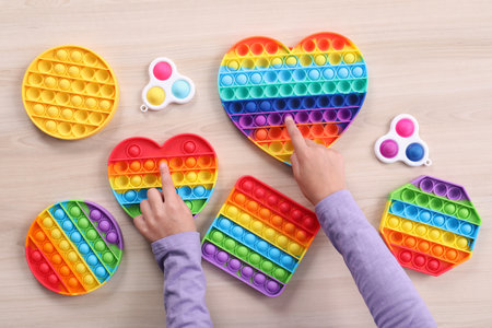Little child playing with pop up and simple dimple fidget toys at wooden table, top view