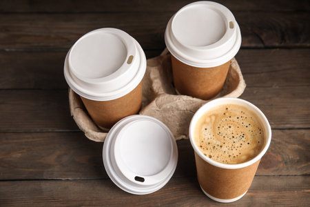 Takeaway paper coffee cups with plastic lids and cardboard holder on wooden tableの写真素材