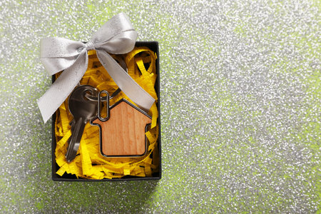 Key with trinket in shape of house, glitter and gift box on shiny surface, top view with space for text. house warming partyの写真素材
