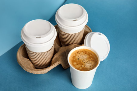 Takeaway paper coffee cups with sleeves, plastic lids and cardboard holder on blue backgroundの写真素材