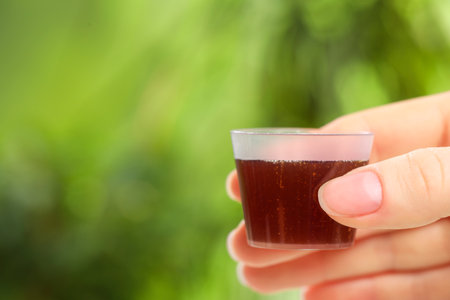 Woman holding measuring cup with syrup on blurred background, closeup and space for text. cold...