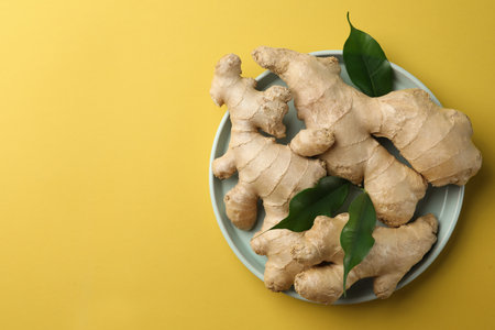 Fresh ginger with green leaves on pale light yellow background, top view. Space for textの写真素材