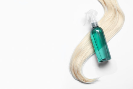 Spray bottle with thermal protection and lock of blonde hair on white background, flat lay. Space for textの写真素材
