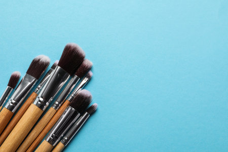 Different makeup brushes on light blue background, flat lay. Space for text