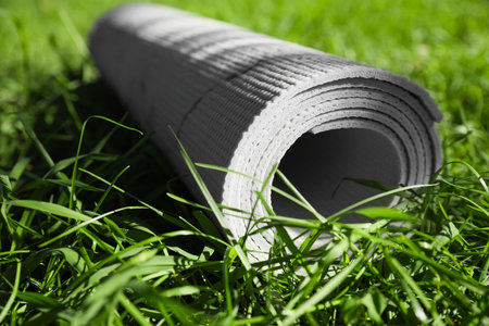 Rolled karemat or fitness mat on green grass outdoors, closeup. Space for textの写真素材