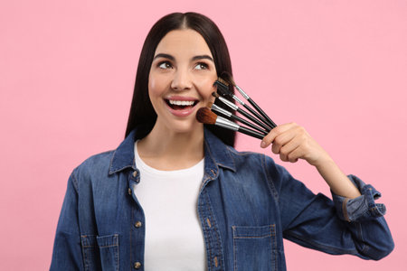 Happy woman with different makeup brushes on pink backgroundの写真素材