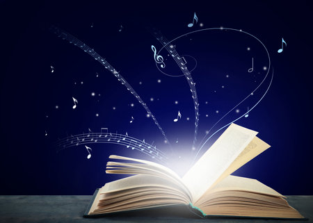 Music flow from book. Musical symbols flying over tome on wooden table against dark blue backgroundの写真素材