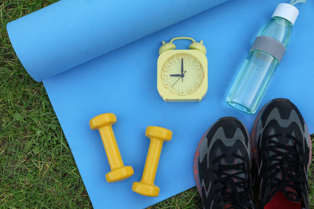 Alarm clock and morning exercise set on green grass, flat layの写真素材