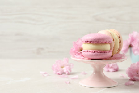 Delicious colorful macarons and pink flowers on light gray table, space for textの写真素材
