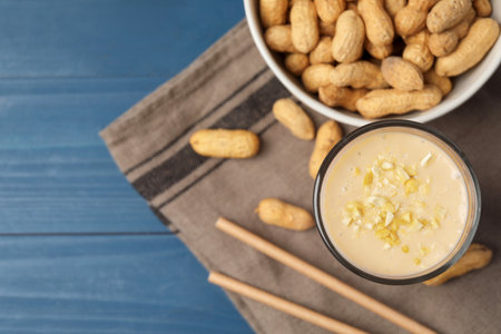 Glass of tasty banana smoothie with peanuts on light blue wooden table, flat lay. Space for textの写真素材
