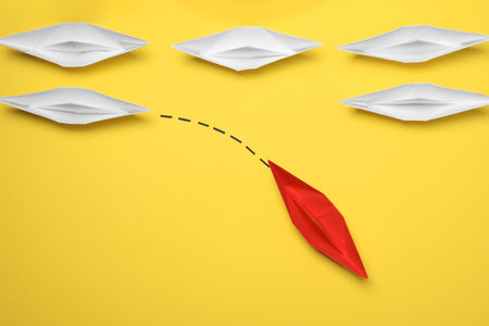 Red paper boat floating away from others on yellow background, flat lay. uniqueness conceptの写真素材