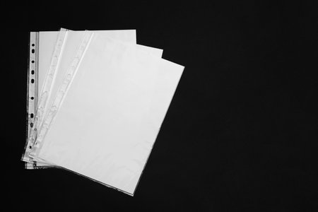 Punched pockets with paper sheets on black background, flat lay. Space for textの写真素材