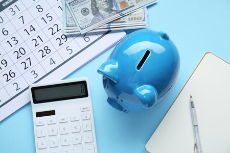 Flat lay composition with piggy bank and calculator on light blue backgroundの写真素材