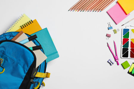 Backpack with different school stationery on white background, flat lay. Space for text