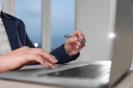 Woman with pen working on laptop at wooden table, closeup. Electronic document managementの写真素材