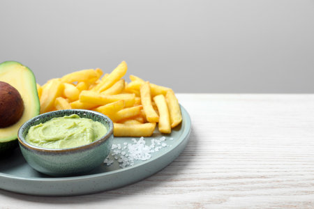 Plate with french fries, guacamole dip and avocado served on white wooden table, space for textの写真素材