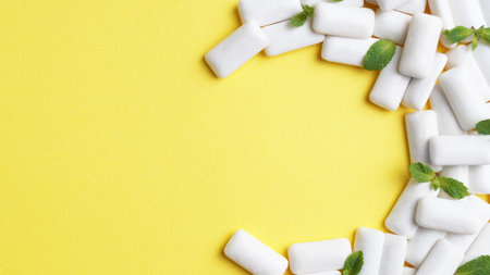 Tasty chewing gums and mint leaves on yellow background, flat lay. Space for textの写真素材