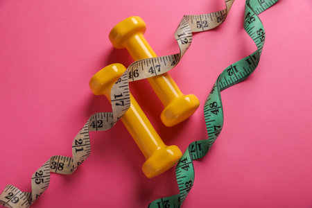 Measuring tapes and dumbbells on pink background, flat lay. weight control conceptの写真素材