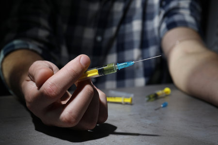 drug addiction. Man with syringe at gray table, closeupの写真素材