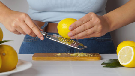Woman grating lemon zest on wooden board at white tiled table, closeupの写真素材