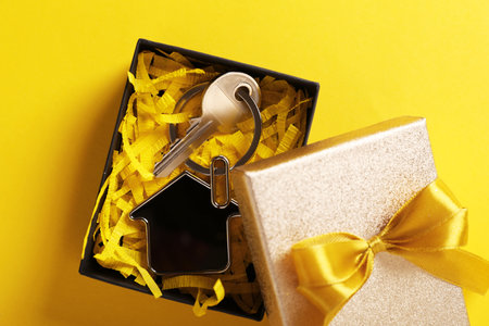 Key with trinket in shape of house and gift box on yellow background, flat lay. house warming partyの写真素材
