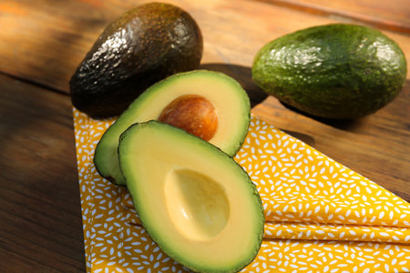 Fresh whole and cut avocados on wooden table, closeup