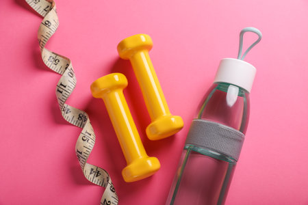 Measuring tape, bottle of water and dumbbells on pink background, flat lay. weight control conceptの写真素材