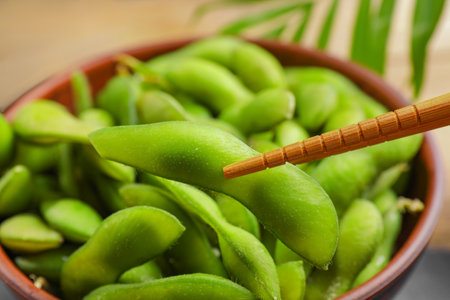 Taking edamame beans in pod from bowl with chopsticks, closeupの写真素材
