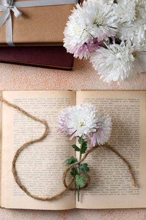 Book with chrysanthemum flowers as bookmark on beige textured background, flat layの写真素材