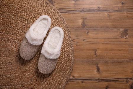 Pair of warm stylish slippers and wicker mat on wooden floor, flat lay. Space for textの写真素材