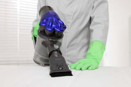 Woman in gloves disinfecting mattress with vacuum cleaner indoors, closeupの写真素材