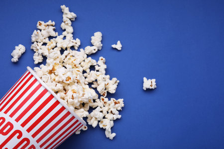 Bucket of tasty popcorn on blue background, flat lay. Space for textの写真素材