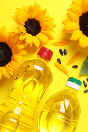 Bottles of cooking oil, sunflowers and seeds on yellow background, flat layの写真素材