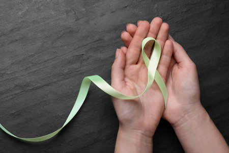 World Mental Health Day. Woman holding green ribbon on black background, top view with space for textの写真素材