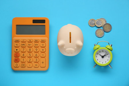 Piggy bank, alarm clock, calculator and coins on light blue background, flat layの写真素材