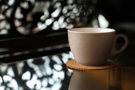 Cup with cork coaster on black table in cafe, closeup. Space for textの写真素材