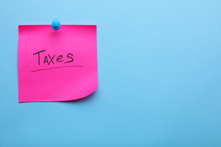 Paper note with word Taxes pinned on light blue background, space for textの写真素材