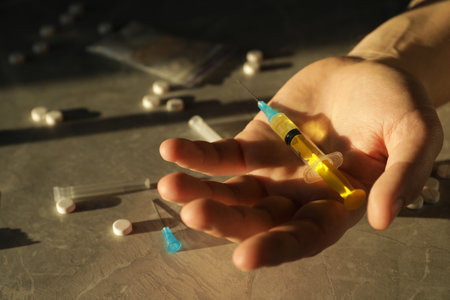 Addicted man holding syringe near drugs at gray textured table , closeupの写真素材