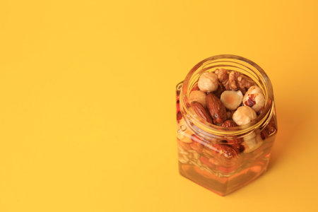 Different nuts and honey in jar on yellow background, above view. Space for textの写真素材