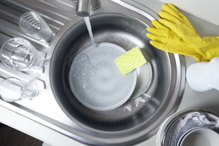 Washing plates, sponge and rubber gloves in kitchen sink, above viewの写真素材