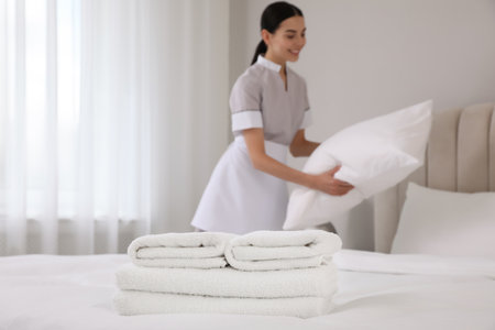 Chambermaid making bed in hotel room, focus on fresh towels. Space for textの写真素材