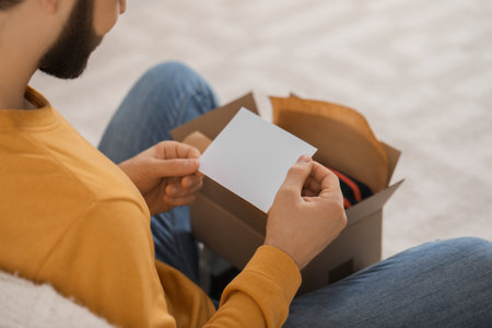Man holding greeting card near parcel with Christmas gift, closeup