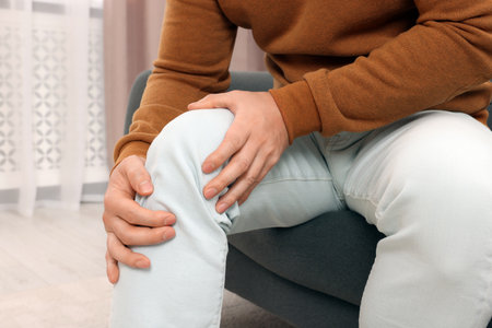 Man suffering from knee pain on sofa indoors, closeupの写真素材