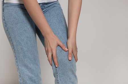 Woman suffering from pain in her knee on light gray background, closeup with space for text....