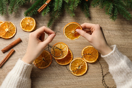 Woman making handmade garland from dry orange slices on wooden table, top viewの写真素材